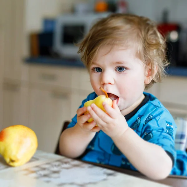 Menina adorável bonito bebê comendo pêra fresca. Filho bebê feliz com fome de um ano segurando frutas. — Fotografia de Stock