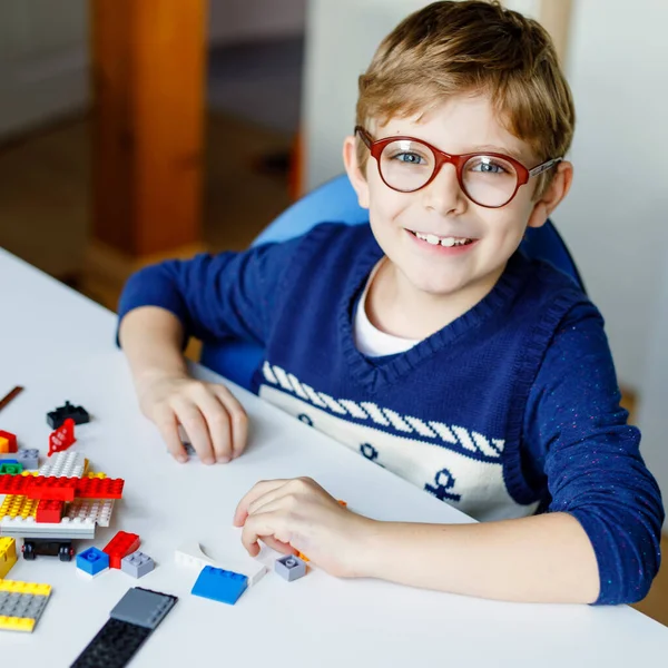 Petit enfant blond avec des lunettes jouant avec beaucoup de blocs en plastique coloré. Adorable écolier qui s'amuse avec la construction et la création de robots. Loisirs créatifs technique moderne et robotique. — Photo