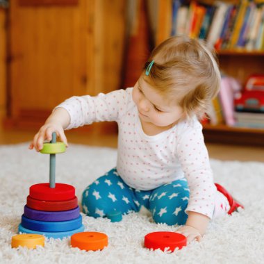 Evde ya da çocuk odasında eğitici tahta oyuncaklarla oynayan sevimli, güzel bir kız bebek. Renkli yığınla piramidi ve müzik oyuncağı olan bir bebek. Mutlu sağlıklı çocuk farklı oyuncaklarla eğleniyor.