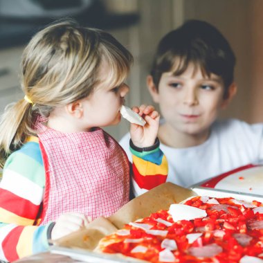 İki kardeş, evde İtalyan pizzası yapan küçük çocuklar. Şirin kız ve okul çocuğu ev mutfağında, evde eğleniyorlar. Erkek ve kız kardeş, aile yemeği hazırlıyor.