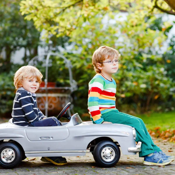 Dos niños preescolares jugando con un gran coche de juguete viejo en el jardín de verano, al aire libre. Los niños felices juegan juntos, conduciendo el coche. Actividad al aire libre para niños. Hermanos y amigos en un día cálido — Foto de Stock