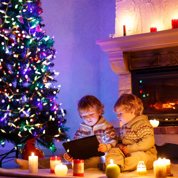 İki sevimli yürümeye başlayan çocuklar, sarışın İkizler yeni tablet hediye ile oynarken. Aile kutluyor Noel tatili — Stok fotoğraf