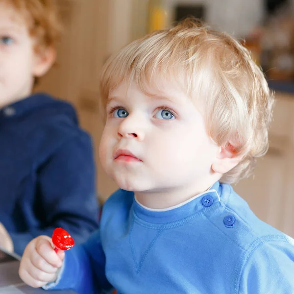 Dva malí batolata, roztomilí bráchové, kteří se dívají na animáky v televizi a jedí bonbóny. Happy siblings together in nursery or nursery, having lunch. — Stock fotografie