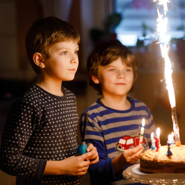 Two beautiful kids, little preschool boys celebrating birthday and blowing candles on homemade baked cake, indoor. Birthday party for siblings children. Happy twins about gifts and fireworks on tarte. — Stock Photo, Image