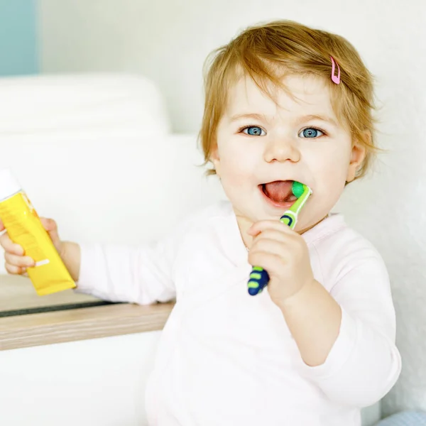 Niña sosteniendo cepillo de dientes y cepillándose los primeros dientes. Niño aprendiendo a limpiar los dientes de leche. Concepto de prevención, higiene y salud. Niño feliz en el baño — Foto de Stock