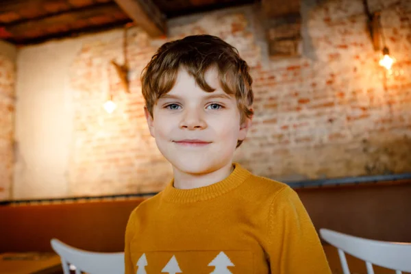 休暇中のレストランでかわいい小学生の少年の肖像画。屋内カフェで幸せな健康な子供. — ストック写真