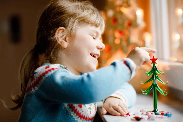 Litte bambina seduta vicino alla finestra e decorare piccolo albero di Natale di vetro con piccoli giocattoli di Natale. Felice bambino sano celebrare la festa tradizionale della famiglia. Adorabile bambino. — Foto Stock