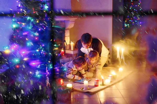 Pai e seus dois filhinhos sentados na chaminé da lareira no tempo da véspera de Natal . — Fotografia de Stock