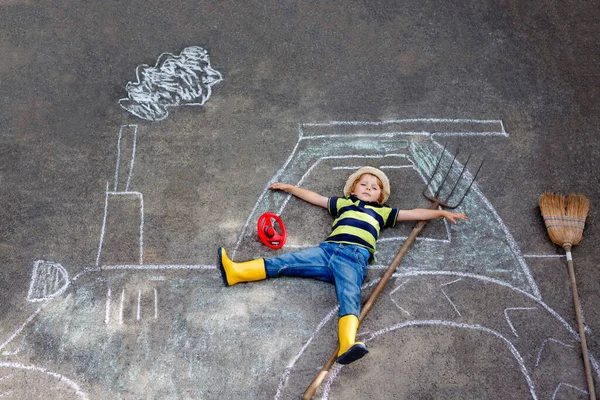 Förtjusande liten pojke leker med färgglada kritor och målar en stor traktorbild på asfalt. Glad förskolebarn leker utanför. Kreativ fritid för barn utomhus på sommaren — Stockfoto