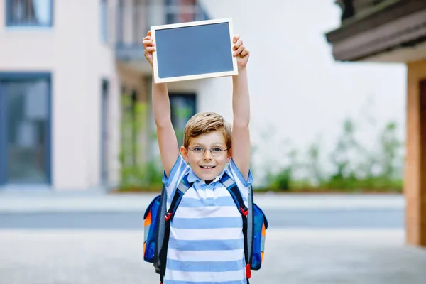 Happy little kid boy with backpack or satchel. Schoolkid on the way to school. Healthy adorable child outdoors With chalk desk for copyspace. Back to school or schools out. — Stock Photo, Image