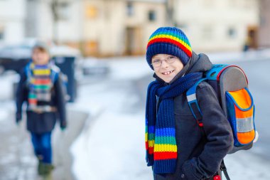 İlköğretim sınıfından iki çocuk kar yağışı sırasında okula yürüyorlar. Mutlu çocuklar eğleniyor ve ilk karla oynuyorlar. Kardeşler, renkli kış kıyafetleri içinde sırt çantalı arkadaşlar..