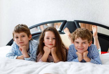Pijamalı üç mutlu çocuk pijama partisini kutluyor. Anaokulu ve okul çocukları ve kız birlikte eğleniyorlar.