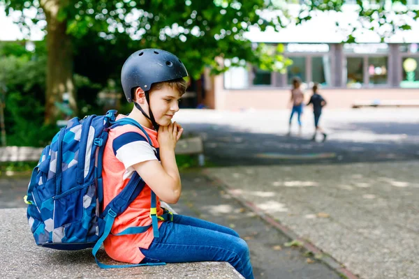 Menino feliz com mochila e capacete de bicicleta. Um estudante a caminho do liceu ou do liceu. Criança adorável saudável ao ar livre no pátio da escola. De volta à escola. Edifício sobre fundo. — Fotografia de Stock