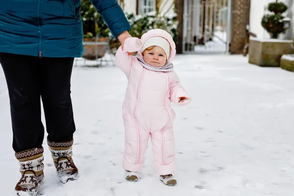 Urocza dziewczynka robi pierwsze kroki na świeżym powietrzu zimą przez śnieg. Słodki maluch uczy się chodzić. Matka trzyma dziecko pod ręką. Córka i mama chodzą razem. Szczęśliwa rodzina — Zdjęcie stockowe