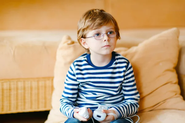 Mignon petit garçon blond avec des lunettes jouant avec une console de jeux vidéo. L'enfant s'amuse à la maison pendant la quarantaine du virus de la couronne. Solitaire garçon seul sans amis, à l'intérieur — Photo