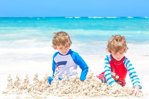 Dwójka małych dzieci bawi się budując zamek z piasku na tropikalnej plaży na wyspie. Zdrowe dzieci bawią się razem na wakacjach. Bliźniaki, Szczęśliwi bracia śmiejący się i uśmiechający — Zdjęcie stockowe