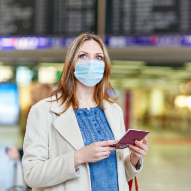 Uluslararası havaalanında maskeli bir kadın elektronik panoyu kontrol ediyor ve uçuş için bekliyor. Coronavirus seyahat kısıtlamaları nedeniyle Avrupa pasaportlu kadın yolcu