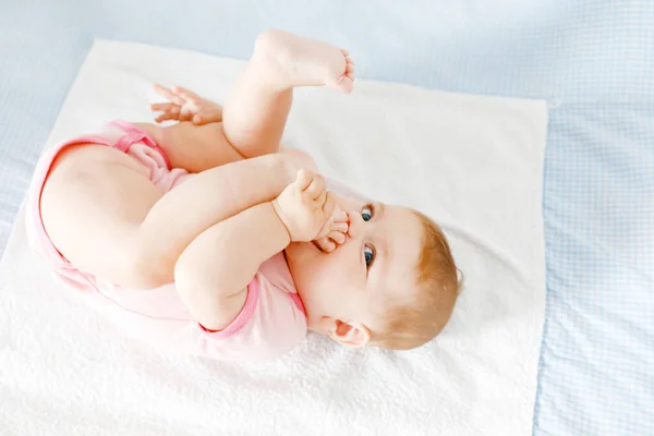 Söt baby tar fötter i munnen. En söt liten flicka som suger på sin egen fot. Glada barn lärande egen kropp — Stockfoto