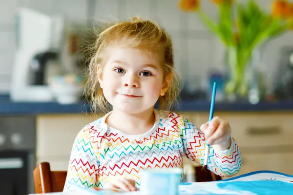 귀엽고 귀여운 여자 애가 물감으로 그림을 배우고 있어. 어린아이들은 화려 한 붓을 사용하여 집에서 그림을 그리고 있다. 건강 한 딸 이 색깔, 집에서 물을 가지고 실험을 하거나 보육원에서 물을 마시는 모습 — 스톡 사진
