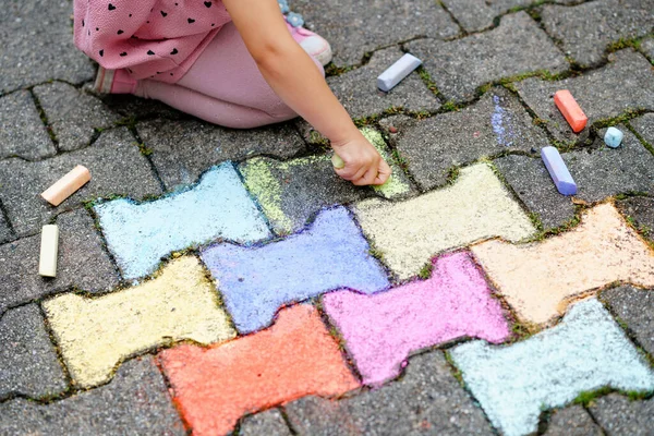 裏庭の地面にカラフルなチョークで小さな就学前の女の子の絵。肯定的な幸せな幼児の子供の絵を描き、絵を作成する。夏の創造的な屋外活動. — ストック写真