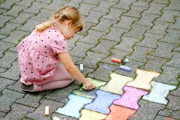 Arka bahçesinde renkli tebeşirlerle resim yapan küçük bir anaokulu kızı. Çocuk resim çizerken ve resim çizerken çok mutlu. Yazın yaratıcı açık hava aktivitesi.