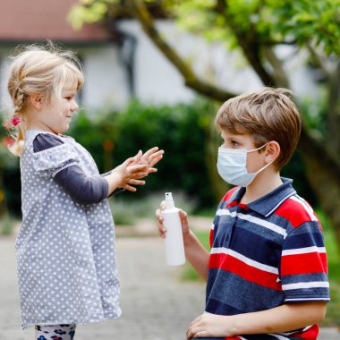 Liseli çocuk küçük kız kardeşine dezenfektanla el temizleme konusunda yardım ediyor. Kardeş ve tatlı küçük kız hijyen kurallarını öğreniyorlar. Coronavirus ve grip salgını sırasında aile. Covid virüs koruması.