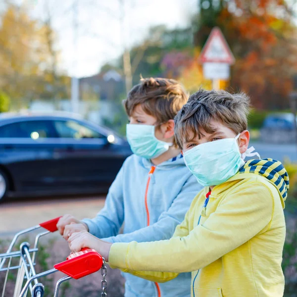 Двоє дітей у медичній масці захищаються від пандемії коронавірусної хвороби. Діти використовують захисне обладнання проти ковадла 19 і йдуть за покупками в супермаркеті з візком . — стокове фото