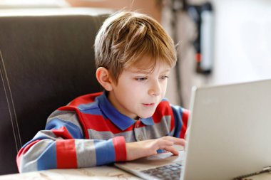 Gözlüklü sağlıklı çocuk evde defteriyle ödev yapıyor. İnternetin yardımıyla ilgili bir çocuk kompozisyon yazıyor. konsept okul çocukları kavramı