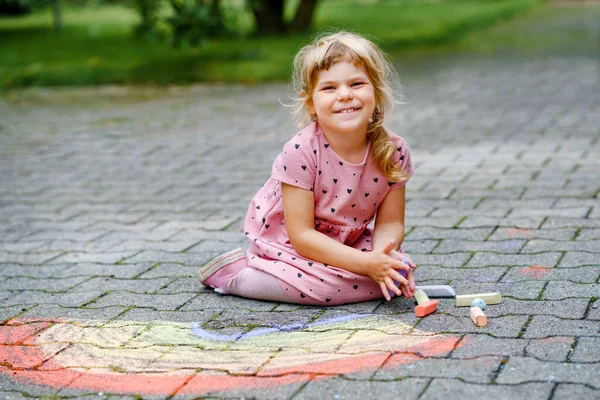 Liten förskola flicka måla regnbåge med färgglada kritor på marken på bakgården. Positivt glad barn rita och skapa bilder. Kreativ friluftsaktivitet på sommaren. — Stockfoto