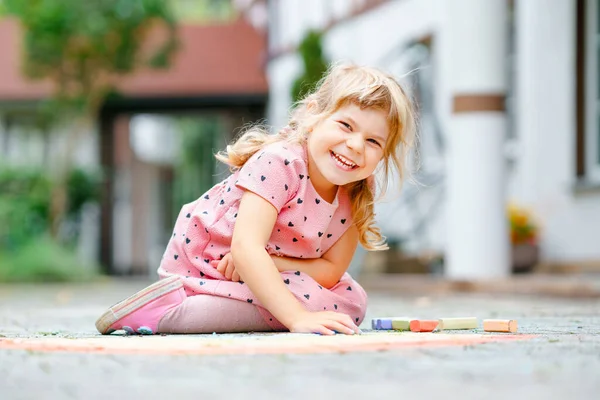 Little preschool girl painting rainbow with colorful chalks on ground on backyard. Positive happy toddler child drawing and creating pictures. Creative outdoors activity in summer. — Stock Photo, Image