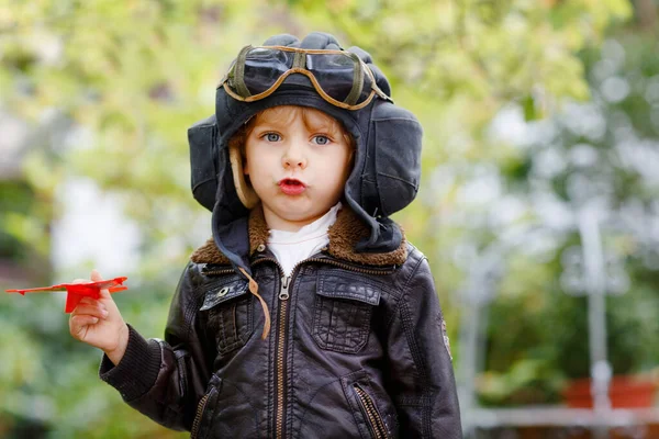 Glad liten pojke i pilothjälm och uniform leker med röda leksaksflygplan. Leende förskolebarn drömmer och har roligt. Utbildning, yrke, drömbegrepp — Stockfoto