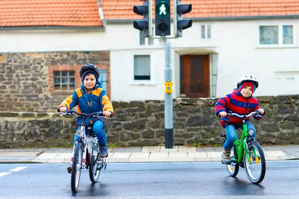 市内の自転車でヘルメットバイクに乗っている2人のアクティブな子供たち。カラフルな服の幸せな子供たちと緑の信号待ち。未就学児の安全と保護 — ストック写真