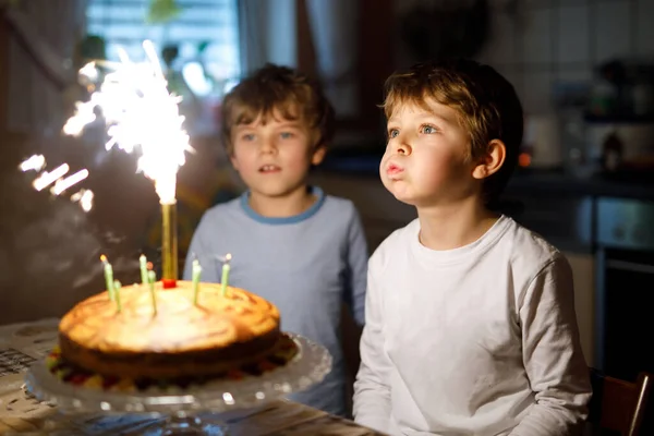 Two beautiful kids, little preschool boys celebrating birthday and blowing candles on homemade baked cake, indoor. Birthday party for siblings children. Happy twins about gifts and fireworks on tarte. — Stock Photo, Image