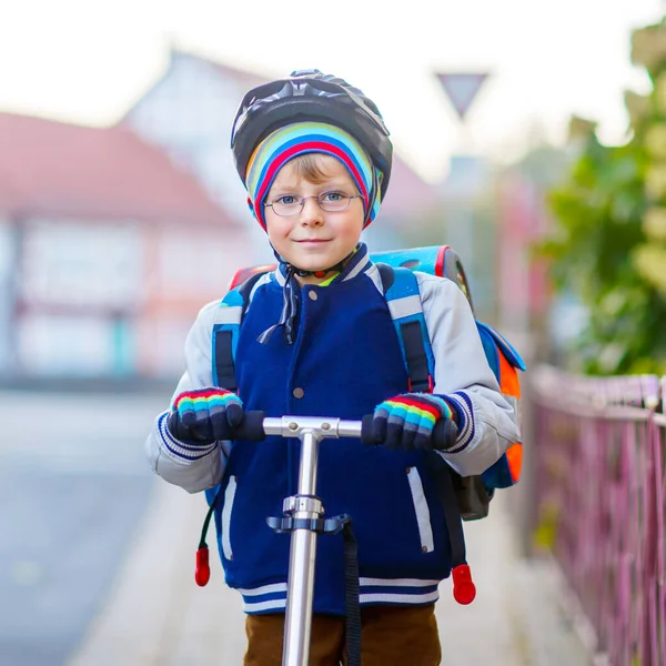 Chłopak w kasku jeździ ze swoim skuterem w mieście. Szczęśliwe dziecko w kolorowych ubraniach na rowerze w drodze do szkoły. Bezpieczny sposób dla dzieci na świeżym powietrzu do szkoły — Zdjęcie stockowe