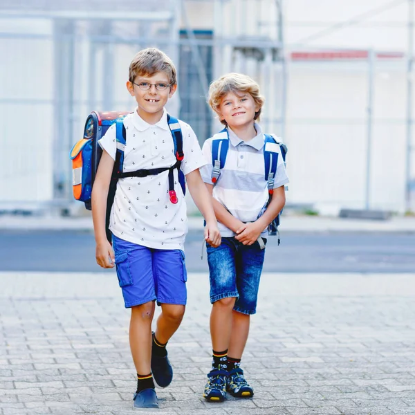 Dwóch małych chłopców z plecakiem lub torbą. Uczniowie w drodze do szkoły. Zdrowe, urocze dzieci, bracia i najlepsi przyjaciele na zewnątrz, opuszczający dom. Wracać do szkoły. Szczęśliwe rodzeństwo. — Zdjęcie stockowe