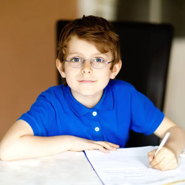 Милый маленький мальчик в очках дома, делает домашнее задание, пишет письма красочными ручками. Маленький ребенок занимается спортом в помещении. Начальная школа и образование, представьте себе фантазию — стоковое фото