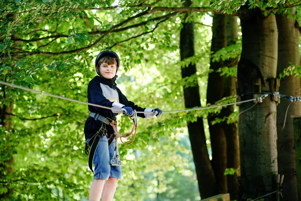 Két gyerek az erdő kalandparkjában. A bukósisakos srácok magas kötélen másznak. Agility készségek és mászás szabadtéri szórakoztató központ gyerekeknek. Szabadtéri tevékenység gyerekeknek és családoknak. — Stock Fotó