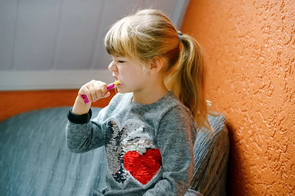 Маленькая дошкольница держит зубную щетку и чистит молочные зубы. Ребёнок учится чистить молочный зуб. Концепция профилактики, гигиены и здравоохранения. Счастливый ребенок в ванной комнате — стоковое фото