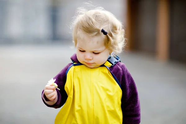 Cute adorable toddler girl playing outdoors on spring day. Baby child wearing yellow mud rain puddle pants trousers. Portrait of happy girl. — Stock Photo, Image