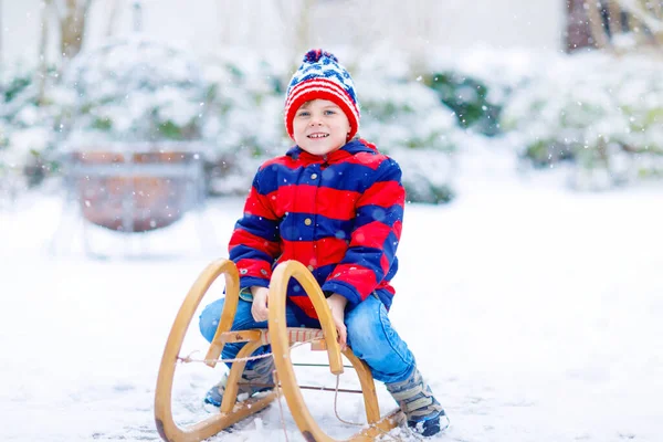 Niño disfrutando de paseo en trineo durante las nevadas. Niño en trineo en la nieve. Niño en edad preescolar montando un trineo. Juego de niños al aire libre. Los niños trineo en el parque de invierno nevado. Diversión activa para vacaciones de Navidad en familia — Foto de Stock