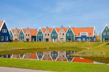 Hollanda 'da Volendam' da aile dostu bir banliyö mahallesinde su kenarında modern tuğlalı evler. Tipik Hollanda evleri ve arka planda yel değirmeni.