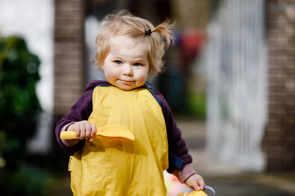 Söt söt liten flicka leker med sand och spade på vårdagen. Barnet bär gula stövlar och lera regnpöl byxor. Lycklig flicka plantera grönsaker på våren. — Stockfoto