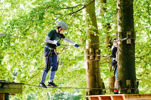 Duas crianças no parque de aventura florestal. Crianças meninos de capacete sobe em trilha corda alta. Habilidades de agilidade e escalada centro de diversões ao ar livre para crianças. Atividades ao ar livre para crianças e famílias. — Fotografia de Stock