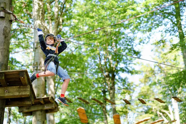 Skolpojke i skogen äventyrspark. Acitve barn, unge i hjälm klättrar på hög rep spår. Agility färdigheter och klättring utomhus nöjescentrum för barn. Friluftsaktivitet för barn och familjer. — Stockfoto