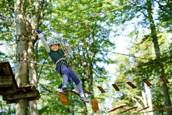 Skolpojke i skogen äventyrspark. Acitve barn, unge i hjälm klättrar på hög rep spår. Agility färdigheter och klättring utomhus nöjescentrum för barn. Friluftsaktivitet för barn och familjer. — Stockfoto