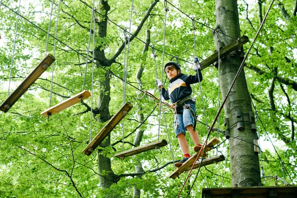 숲 모험 공원에 다니는 남학생. 안전띠를 매고 높은 밧줄 길을 오르는 꼬마 야. 민첩 한 기술 과 아이들을 위한 야외 놀이 센터에 오르기. 어린이와 가족을 위한 옥외 활동. — 스톡 사진