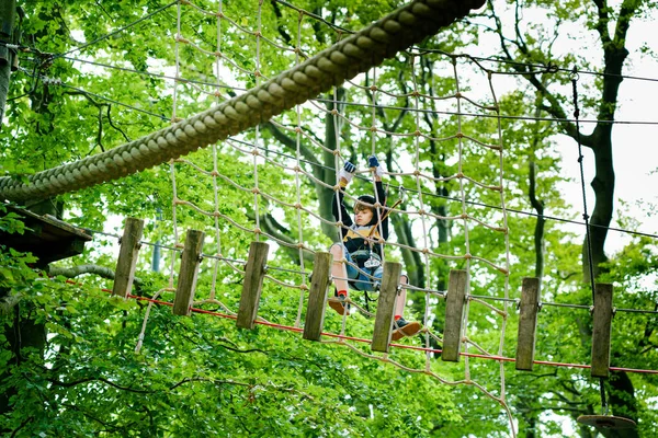 School jongen in bos avonturenpark. Actief kind, kind met helm klimt op een touwenparcours. Agility vaardigheden en klimmen outdoor amusement centrum voor kinderen. Buitenactiviteiten voor kinderen en gezinnen. — Stockfoto