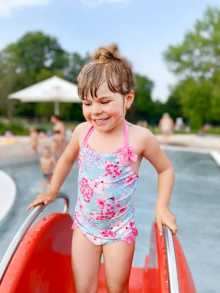Niña preescolar salpicando en una piscina al aire libre en el cálido día de verano. Feliz niño sano disfrutando de un clima soleado en la piscina pública de la ciudad. Actividad infantil al aire libre con agua. — Foto de Stock