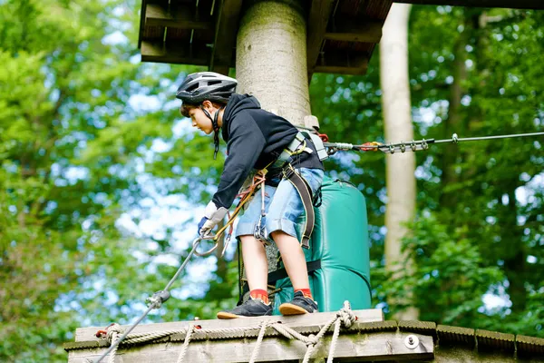 Uczeń w parku przygód leśnych. Kwaśne dziecko, dzieciak w kasku wspina się po szlaku linowym. Umiejętności zręcznościowe i wspinaczka na zewnątrz centrum rozrywki dla dzieci. Działalność na świeżym powietrzu dla dzieci i rodzin. — Zdjęcie stockowe