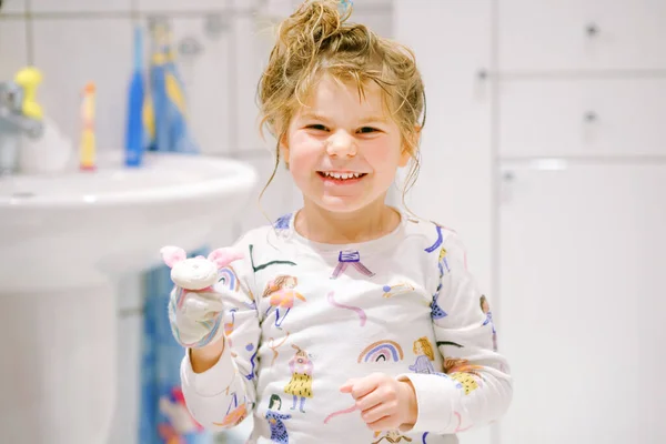 Roztomilá školačka v pyžamu po koupeli. Šťastné usměvavé dítě s mokrými dlouhými vlasy, hrající si s ponožkami, baví. Zdravá hygienická rutina pro děti. — Stock fotografie